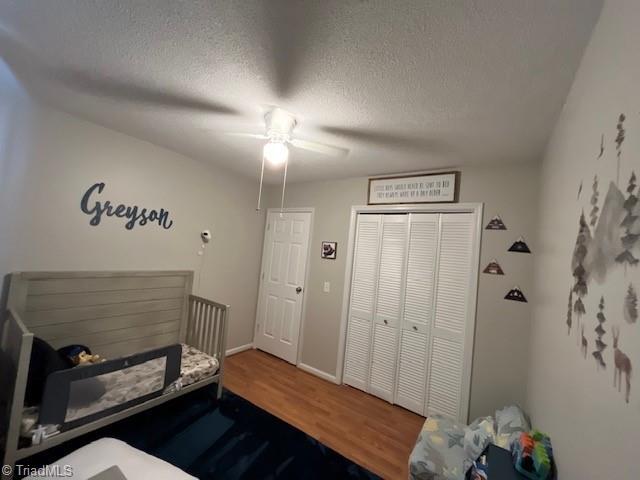 bedroom with a textured ceiling, ceiling fan, wood finished floors, a closet, and a crib