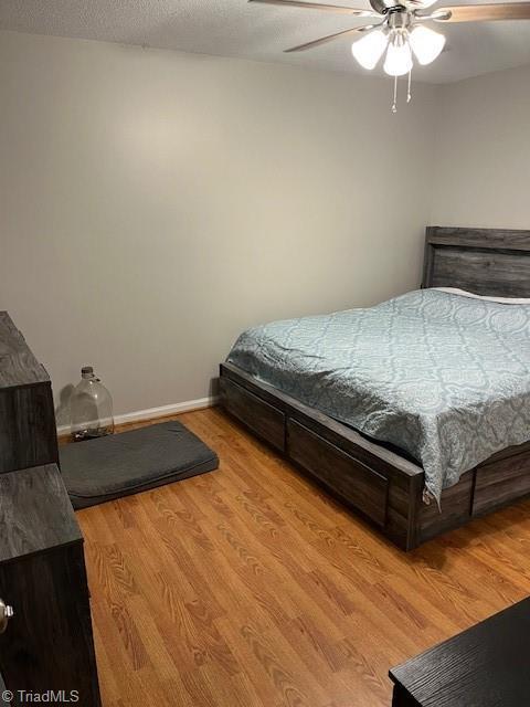 bedroom with ceiling fan, a textured ceiling, wood finished floors, and baseboards