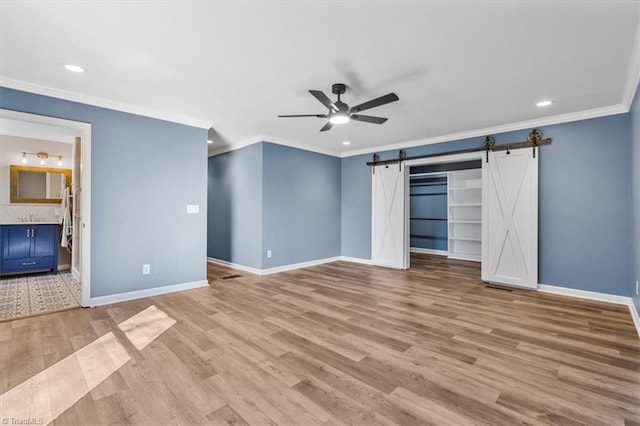 unfurnished bedroom with light wood finished floors, a barn door, ornamental molding, and baseboards