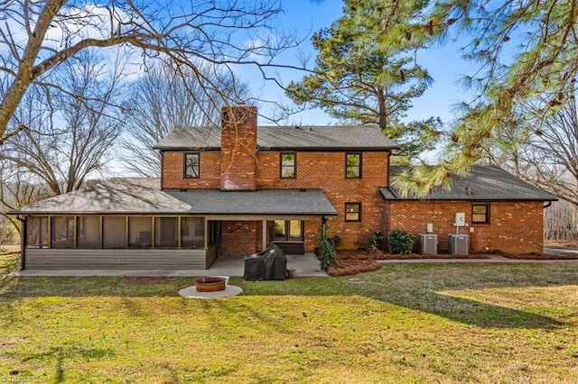 rear view of property featuring a fire pit, a sunroom, a chimney, a yard, and brick siding