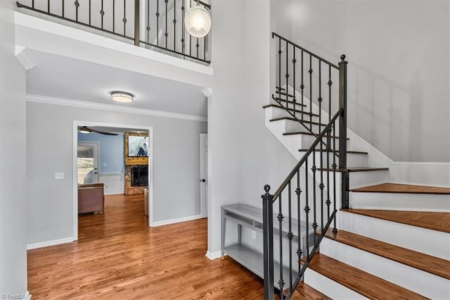 stairs featuring crown molding, a fireplace, baseboards, and wood finished floors