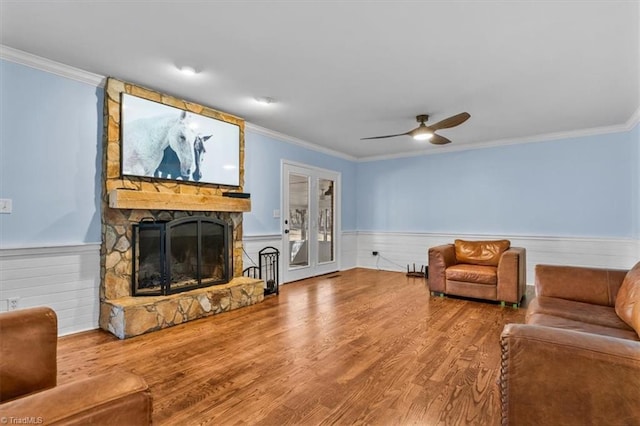 interior space featuring ornamental molding, wainscoting, a stone fireplace, and wood finished floors