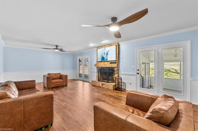 living room with a ceiling fan, a wainscoted wall, ornamental molding, wood finished floors, and a fireplace