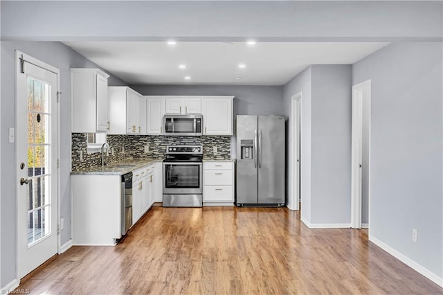 kitchen featuring light wood finished floors, backsplash, appliances with stainless steel finishes, and white cabinetry