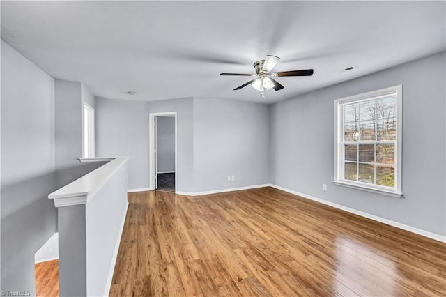 empty room featuring visible vents, a ceiling fan, baseboards, and wood finished floors