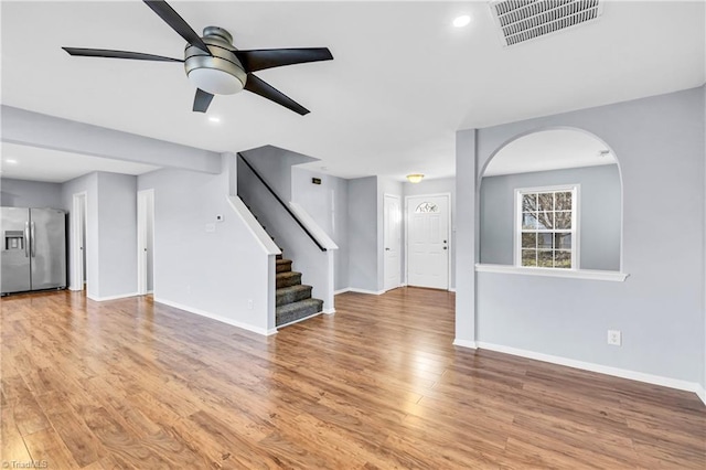 unfurnished living room featuring stairway, visible vents, baseboards, ceiling fan, and light wood-style floors