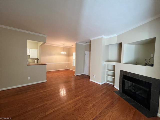 unfurnished living room with built in shelves, dark hardwood / wood-style floors, crown molding, and a tiled fireplace