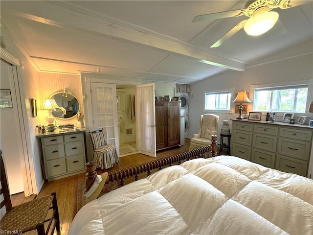 bedroom with ensuite bath, wood finished floors, stacked washer / dryer, ceiling fan, and vaulted ceiling with beams