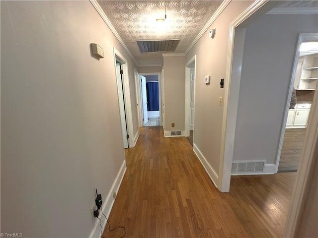 hallway featuring visible vents, baseboards, crown molding, and wood finished floors