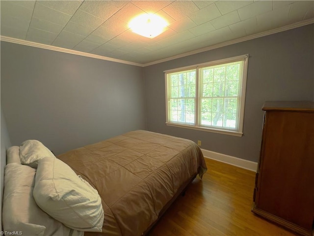 bedroom featuring baseboards, ornamental molding, and wood finished floors
