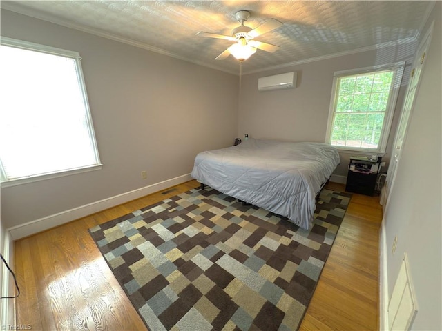 bedroom with a wall unit AC, a ceiling fan, crown molding, baseboards, and light wood finished floors