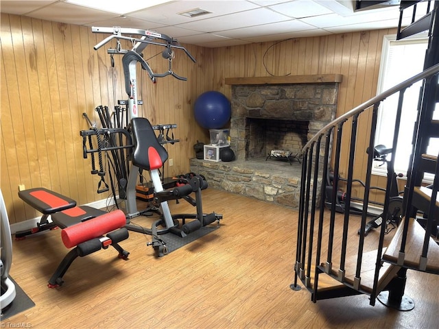 exercise area featuring visible vents, a fireplace, wood walls, wood finished floors, and a drop ceiling
