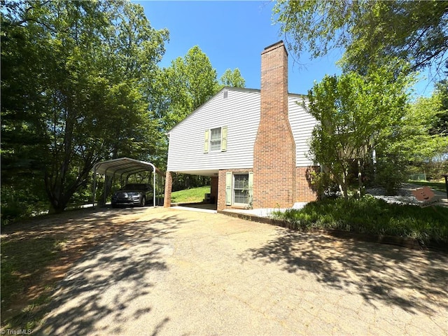 view of home's exterior featuring a detached carport, a chimney, driveway, and brick siding