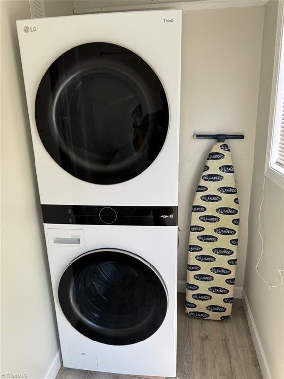 laundry room featuring stacked washer and clothes dryer and hardwood / wood-style flooring