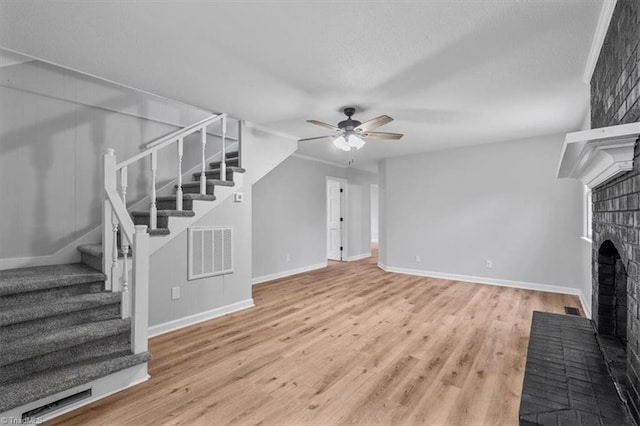 unfurnished living room featuring visible vents, ceiling fan, wood finished floors, stairs, and a fireplace