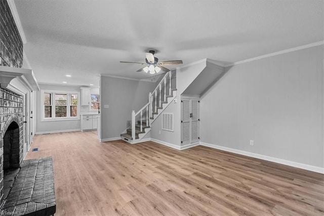 unfurnished living room featuring ceiling fan, a fireplace, stairway, light wood-type flooring, and crown molding