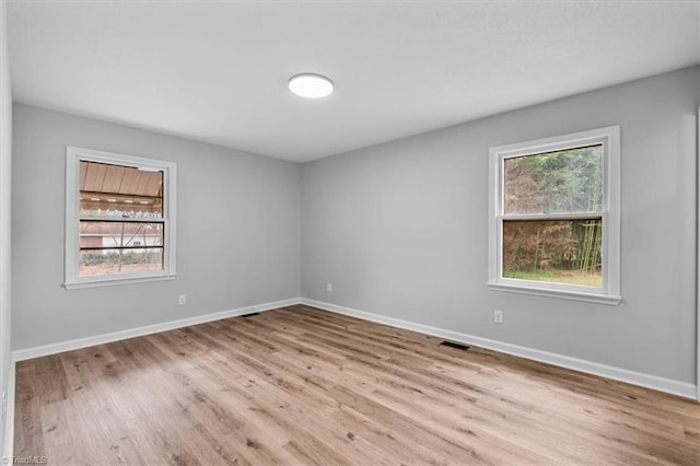 empty room with wood finished floors, visible vents, and baseboards