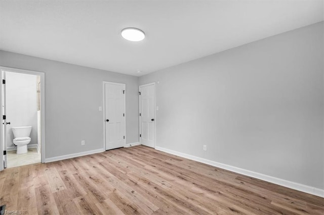 unfurnished bedroom with connected bathroom, baseboards, and wood finished floors