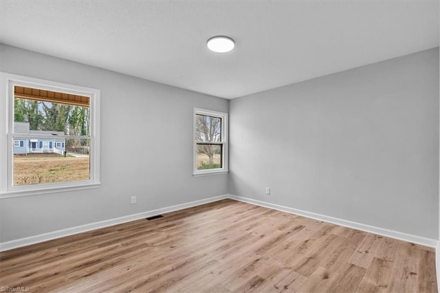 empty room featuring wood finished floors, visible vents, and baseboards