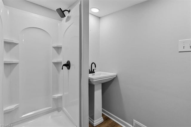 bathroom with a sink, wood finished floors, walk in shower, and baseboards