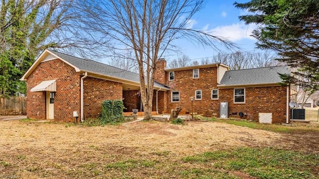 rear view of house featuring brick siding, fence, and a chimney