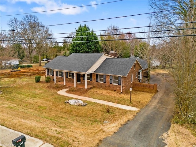 ranch-style house with driveway, roof with shingles, covered porch, a front lawn, and brick siding