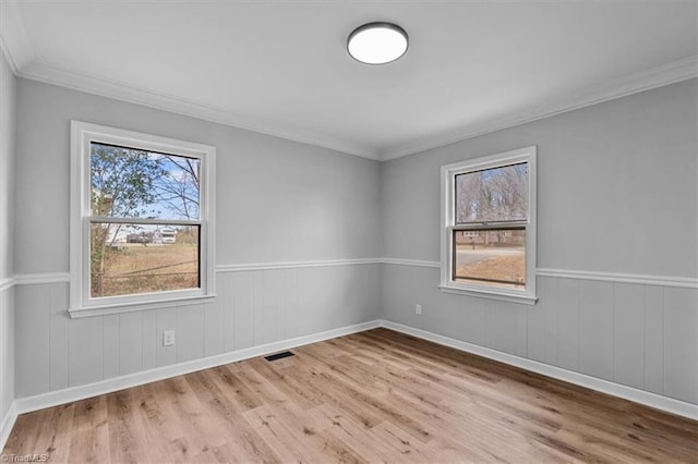 unfurnished room featuring a wealth of natural light, wainscoting, and wood finished floors