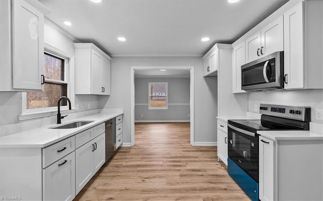 kitchen with stainless steel appliances, light countertops, white cabinetry, a sink, and baseboards