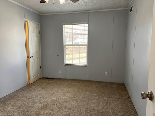 carpeted empty room with ceiling fan, ornamental molding, a healthy amount of sunlight, and a textured ceiling