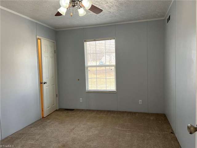 carpeted spare room with ceiling fan, a wealth of natural light, ornamental molding, and a textured ceiling