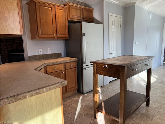 kitchen with light tile patterned floors, ornamental molding, and stainless steel refrigerator