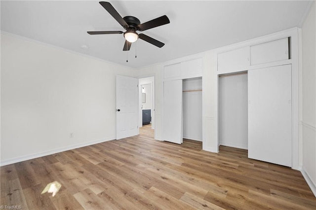 unfurnished bedroom featuring two closets, crown molding, ceiling fan, baseboards, and light wood-type flooring