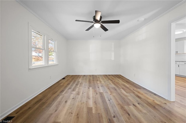 spare room featuring visible vents, a ceiling fan, crown molding, light wood finished floors, and baseboards