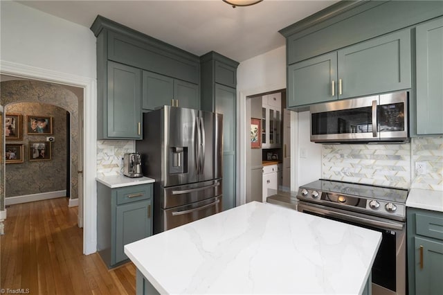 kitchen with wood finished floors, baseboards, appliances with stainless steel finishes, tasteful backsplash, and a center island