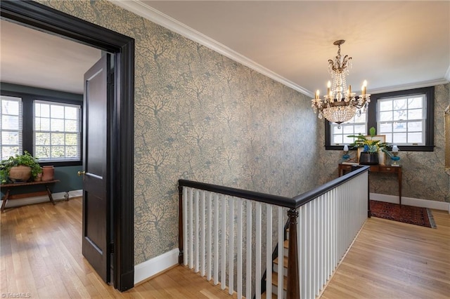 hall featuring wood finished floors, a healthy amount of sunlight, wallpapered walls, and ornamental molding