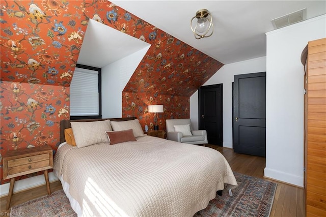 bedroom with wallpapered walls, vaulted ceiling, wood finished floors, and visible vents