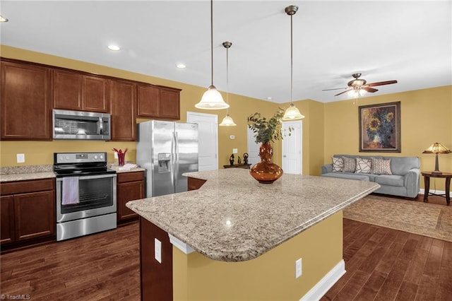 kitchen featuring light stone countertops, ceiling fan, a center island, stainless steel appliances, and dark wood-style floors