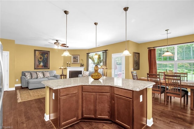 kitchen featuring dark wood-style flooring, hanging light fixtures, a fireplace, a ceiling fan, and baseboards