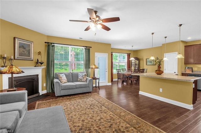 living room featuring a fireplace with flush hearth, baseboards, ceiling fan, and dark wood finished floors