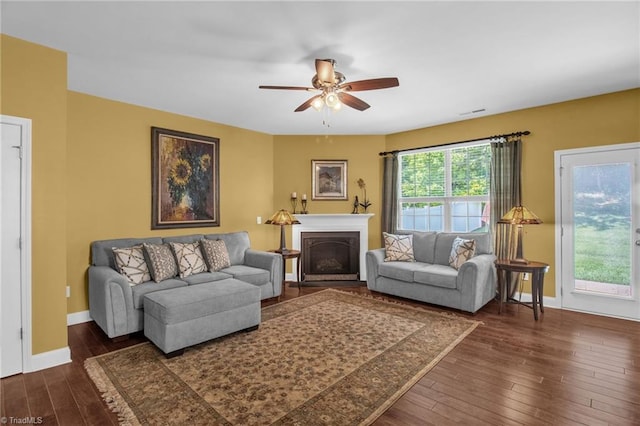 living area with baseboards, a fireplace, a ceiling fan, and dark wood-style floors