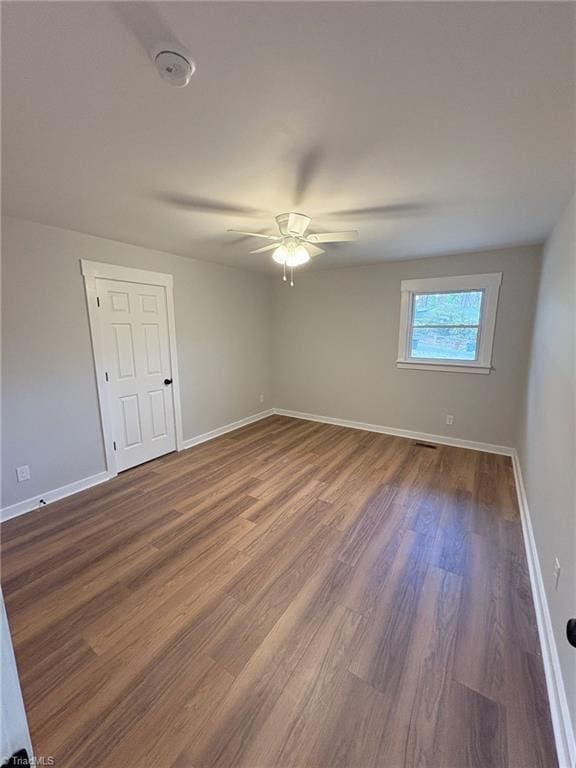 spare room featuring ceiling fan, baseboards, and dark wood-type flooring