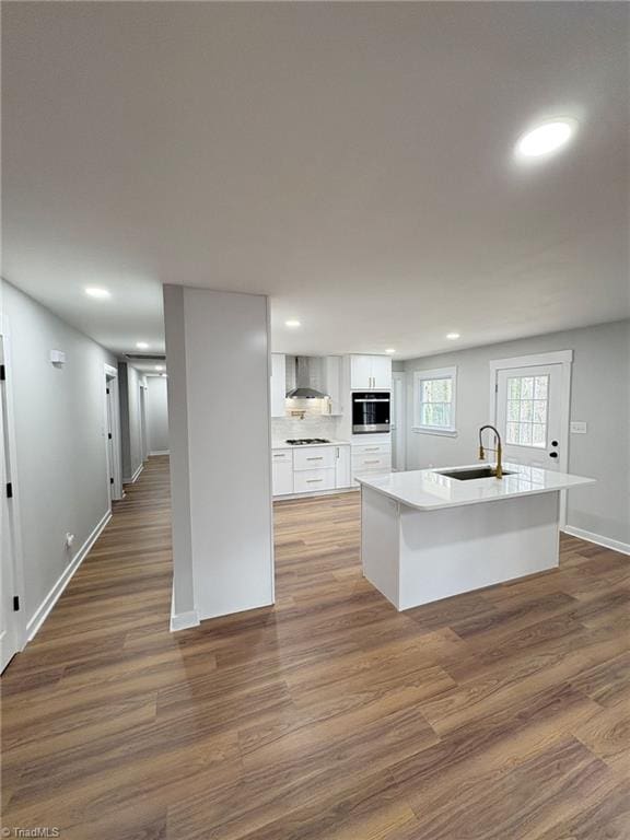 kitchen featuring wood finished floors, wall chimney range hood, a sink, and white cabinets