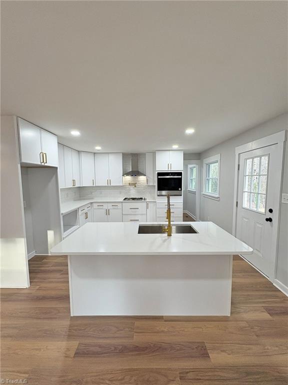 kitchen featuring stainless steel oven, dark wood-type flooring, a sink, and wall chimney range hood