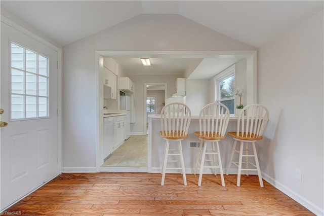 dining area with light wood-style flooring, baseboards, and vaulted ceiling