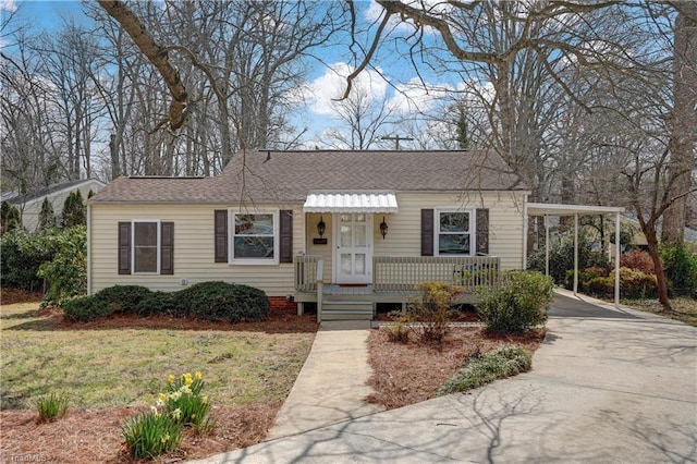 view of front of house with a carport, concrete driveway, a front lawn, and a shingled roof