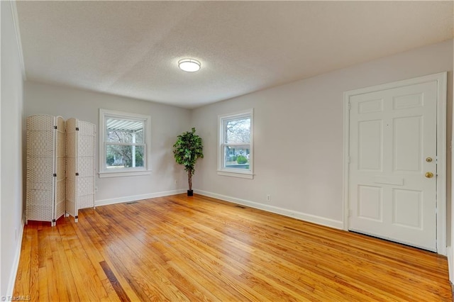 spare room featuring plenty of natural light, a textured ceiling, light wood-type flooring, and baseboards