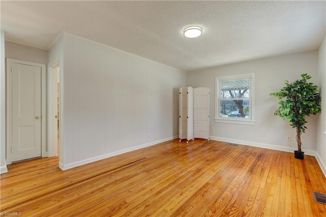 empty room with light wood-style flooring, visible vents, baseboards, and a textured ceiling