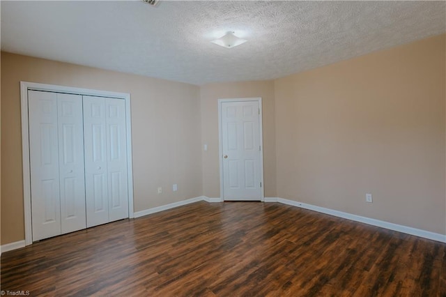 unfurnished bedroom with a textured ceiling, a closet, baseboards, and dark wood-style flooring