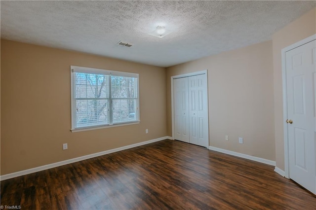 unfurnished bedroom featuring a textured ceiling, dark wood-type flooring, visible vents, baseboards, and a closet