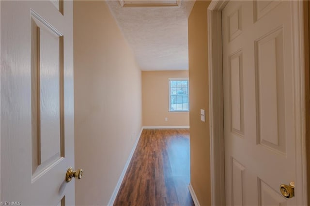 hall featuring a textured ceiling, dark wood-style flooring, and baseboards